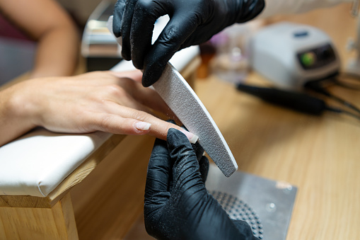 Close-up of a technician polishing the nails of a client using a file in a salon