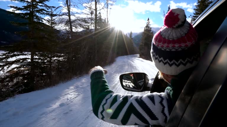 Young man outstretches arm from inside car on snowy mountain road- road trip