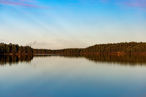 Lake Saimaa in Finland on a spring morning. Serene landskape with mirror calm water surface. Some fluffy clouds reflecting from the lake surface. Clear water and stones can be seen.
