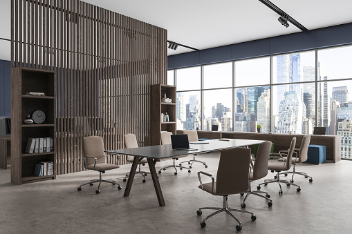 Modern blue office interior with armchairs and laptop on desk, side view shelf partition with decoration. Business meeting and coworking corner, panoramic window on New York. 3D rendering