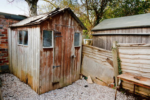 badly maintained old aged run down burlap panel wooden garden shed with damaged roof and hole from wood rot