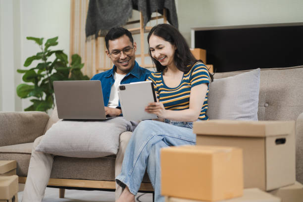 istock Young couple relaxing sitting on the sofa using the computer laptop around cardboard boxes, very happy moving to a new house. 1736759803