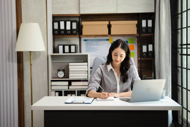 istock Confident beautiful Asian businesswoman typing laptop computer and digital tablet while holding tablete at office 1736764831