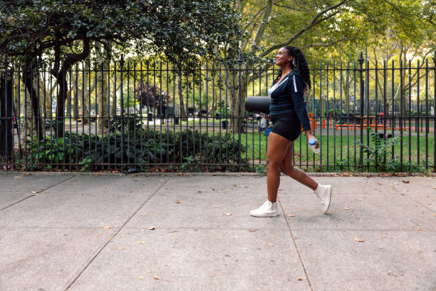 Woman going to sport training class holding a yoga mat Healthy woman walking in New York going to the park for a outdoors training class. harlem park stock pictures, royalty-free photos & images