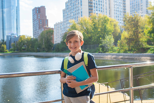 Portrait of a smiling schoolboy with backpack and books on the background of the city