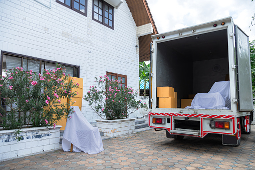 Background of cargo truck stop near house with many cardboard boxes and furniture waiting to move goods to new house, professional services logistic business moving house industry company concept
