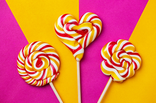 Three large lollipops on a stick in the shape of a circle, a flower and a heart on a bright orange-purple background, handmade. close-up