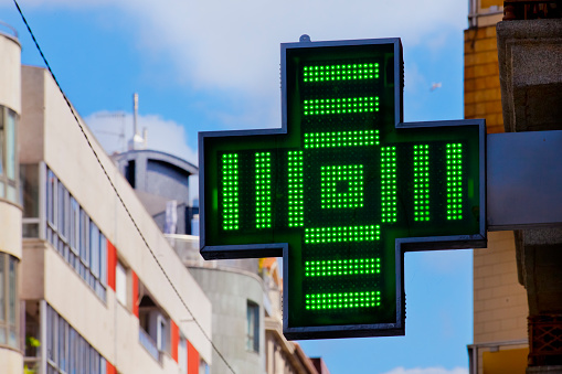 Pharmacy symbol in the street,green cross, small part of residential building facades, clear blue sky background . Copy space on the left. Galicia, Spain.