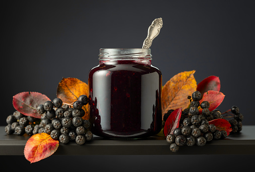 Chokeberry jam and fresh berries with leaves on a black background.