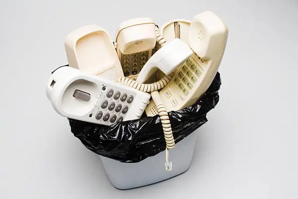"Landline telephones in a wastepaper basket, handsets and bases, white and beige, dangling phone cord, against gray backgroundOther telephones in waste basket photos"