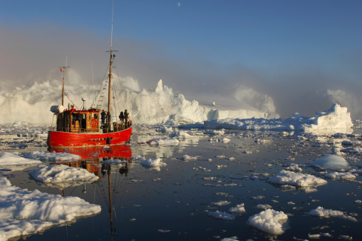 A red boat enters the iceberg choked Ice fjord at Ilulissat in Greenland inside the Arctic Circle