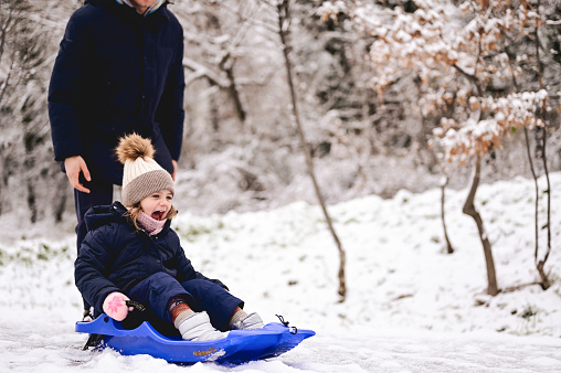 Multiracial preschool age girl of Chinese and Hawaiian descent smiles and laughs up toward the camera while laying on her back in the snow and making snow angel during a cold, winter day at home.