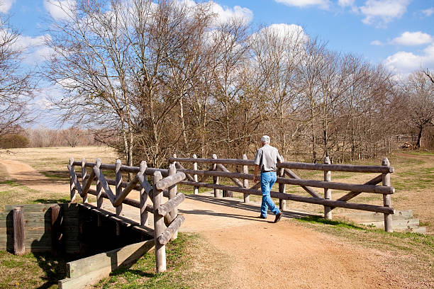 Man walking over rural bridge to old farmplace.