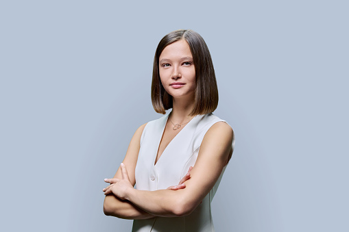 Portrait of young confident woman on grey studio background. Successful fashionable female with crossed arms looking at camera. Business, work, services, education, fashion beauty professions
