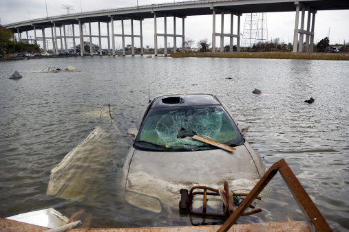 A flooded car sits hopelessly submerged near an overpass.