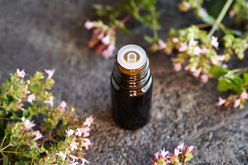 Aromatherapy essential oil in a brown glass bottle with blooming oregano plant