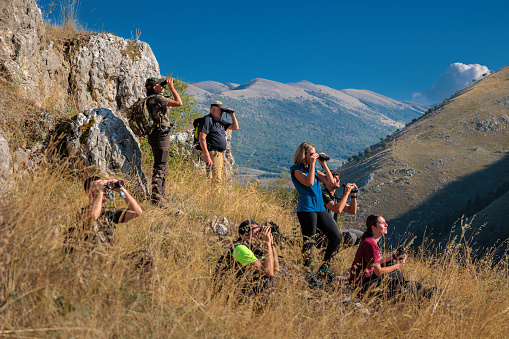 Bisegna (AQ), Italy - October 8, 2023: Group of hikers in the mountains observes wild animals in nature with binoculars.