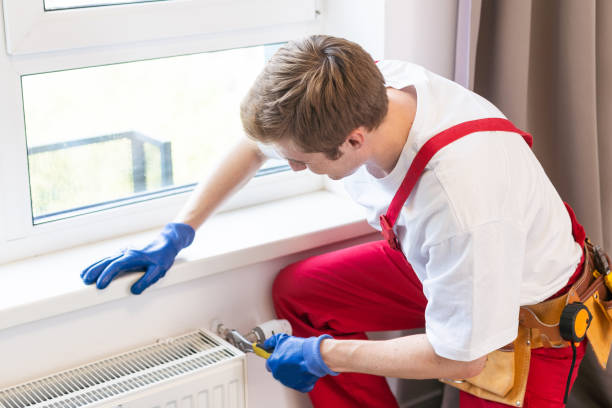 istock Young handsome professional plumber worker installing heating radiator in an empty room of a newly built apartment or house. Construction, maintenance and repair concept 1736961631