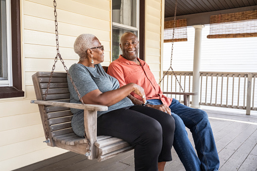 Three-quarter front view of casually dressed couple in late 60s side by side, talking and smiling as they enjoy summer day outdoors.