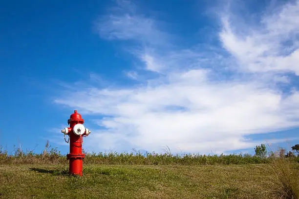 Red fire hydrant on a hill against a love blue sky with whispy clouds.  Great copy space.