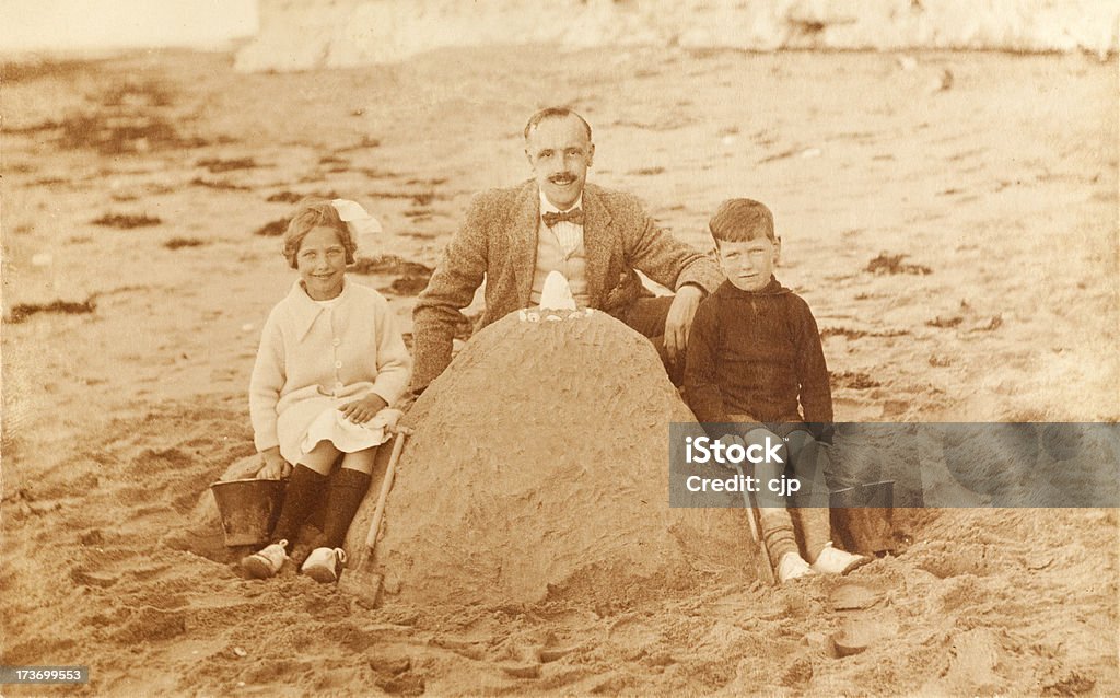 Father and Children at Beach Vintage sepia photograph of a father and his children by a large sandcastle at the beach in 1920's. Some dust and scratches that reflect age of image. 1920-1929 Stock Photo