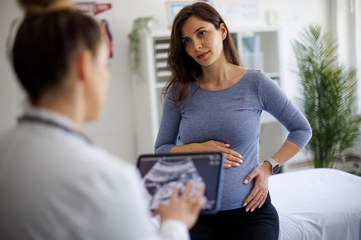 A female doctor explaining an ultrasound scan of a baby to a worried pregnant woman using a digital tablet during a medical consultation