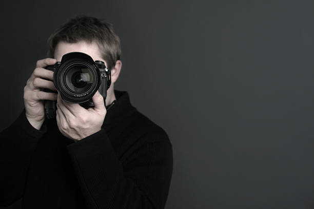 Portrait of a photographer with camera in front of his face A photographer with a nice camera.  Focus is on the lens. slr camera photos stock pictures, royalty-free photos & images