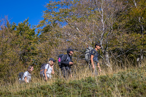 Bisegna (AQ), Italy - October 8, 2023: Group of hikers with backpacks walking up the mountain. Autumn season.