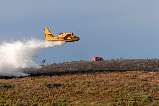 A twin-engined water bomber dumping its load on a forest fire