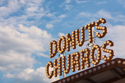A sign on top of kiosk where donuts and churros are for sale.
