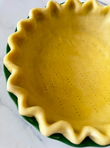 Stock photo showing close-up, elevated view of a freeform fluted, pastry dough lining of a tart tin case that has been pricked with a metal fork, in preparation of baking a pie. Homemade pastry made with white flour and butter ready to be blind baked and filled with a savoury or sweet sauce. Home baking concept.