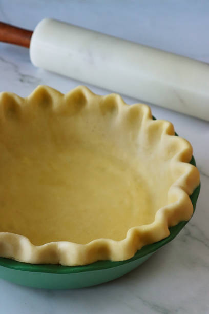 istock Close-up image of pricked pastry dough lined tart tin case, marble rolling pin, freeform fluted pie crust, preparation for blind baking pie, homemade pastry made of white flour, marble effect background, elevated view, focus on foreground 1737067068