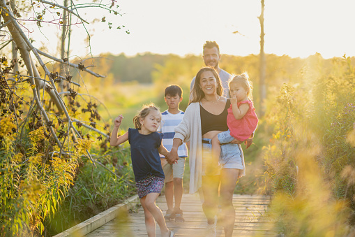 A small mixed race family is seen taking a walk together at sunset on a warm fall day.  They are each dressed casually as they enjoy the fresh air and each others company.
