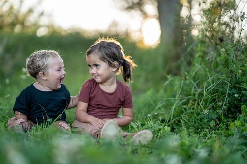 Two cute little sisters having fun while laying in the grass on a sunny summer day