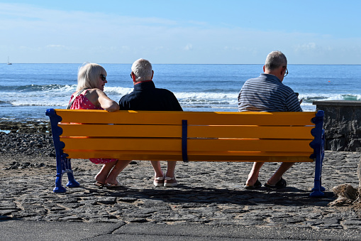 Young couple relaxing on park bench by the beach watching sunset. People love and relationships concept.