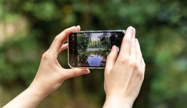 istock Hands holding smartphone, taking mobile photo, capturing nature, forest and lake 1737095194