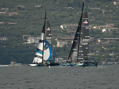 TF35 class catamarans Spindrift team and Realteam Sailing team seen from the side with the town in the background. Malcesine Cup 09/2023. Malcesine, Italy.