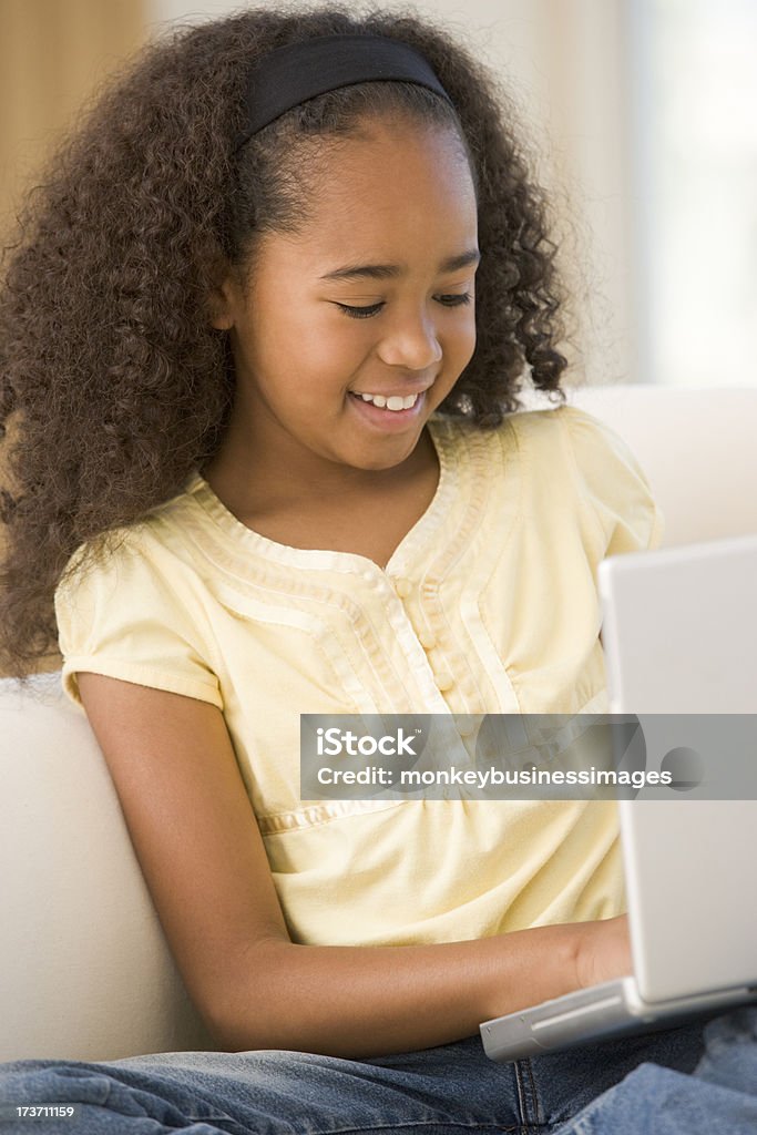 Jovem garota usando o laptop na sala de estar e sorrindo - Foto de stock de Afro-americano royalty-free