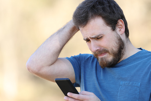 Sad man checking smart phone bad content outdoors