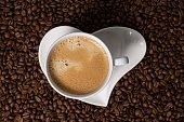 cup of coffee on a saucer in the shape of a heart. Coffee on a background of coffee beans.