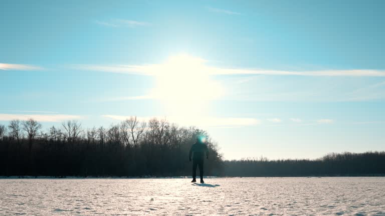 Silhouette of a man walking into the distance through the snow during sunset. A loner walks across a large meadow of snow. Failure and loneliness.