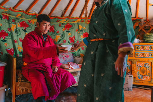 Mongolian woman passing bowl of milk tea to her husband inside yurt