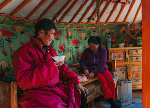 Mongolian man enjoying goat milk tea inside yurt with his family