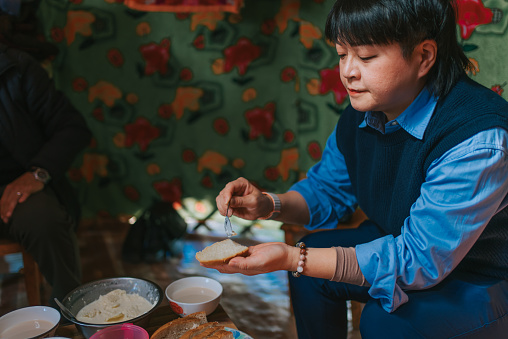 solo travel Asian Chinese woman trying homemade butter with bread inside Mongolian yurt