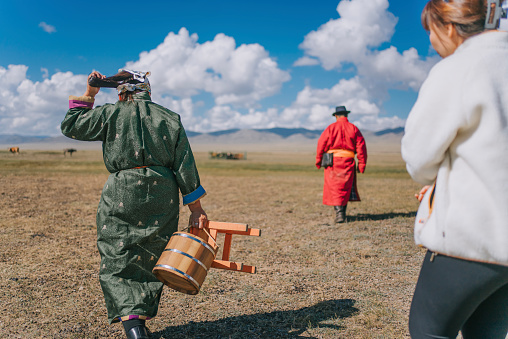 Mongolian couple carrying barrel walking across the pasture to milk the cow