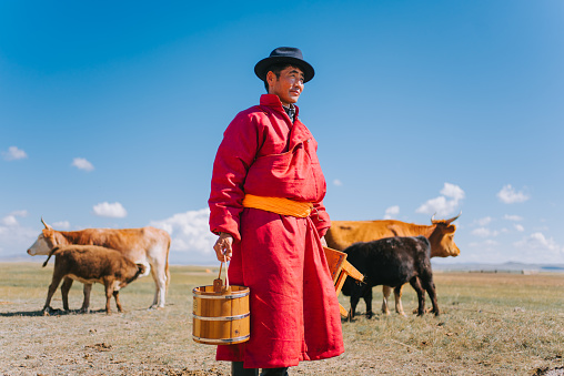 Mongolian man carrying milk bucket looking away standing on pasture