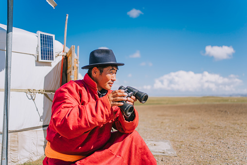 Mongolian nomadic man grazing watching flock of sheeps with binoculars