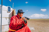 Mongolian nomadic man grazing watching flock of sheeps with binoculars in front of yurt