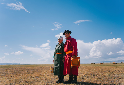 portrait of Mongolian couple standing on pasture carrying milk bucket, stool