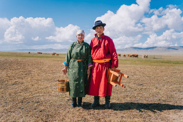 portrait of mongolian couple standing on pasture carrying milk bucket, stool - independent mongolia fotos imagens e fotografias de stock